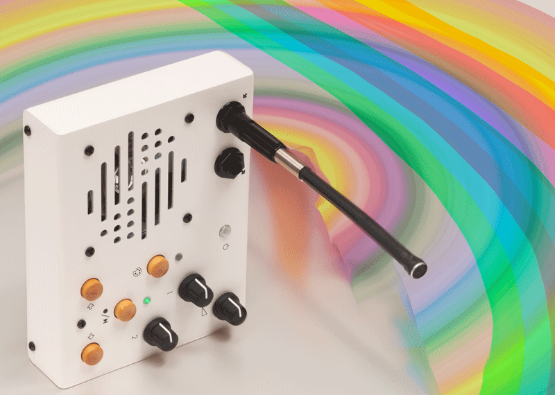 Portable recorder/looper on its side with a rainbow background behind it. White with knobs and wooden buttons, a large speaker grill, and a gooseneck mic protruding perpendicular to the front panel.