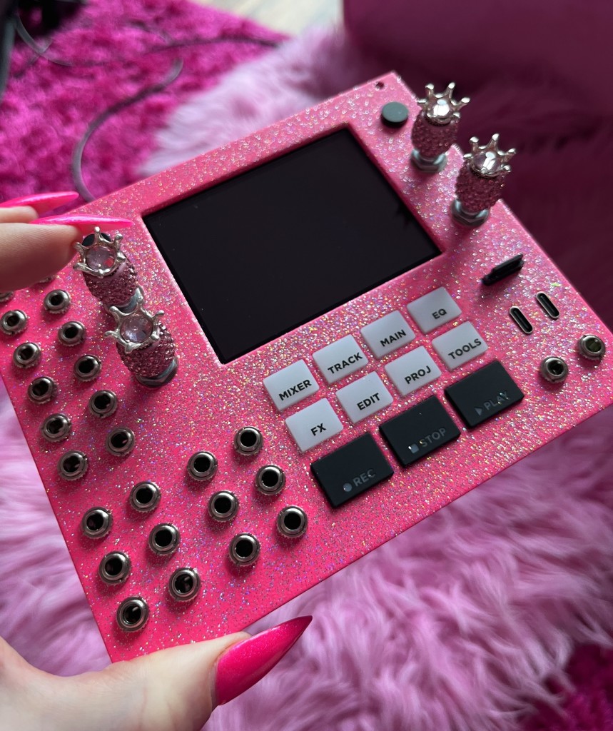 Custom pink 1010music Bluebox Eurorack Edition – Compact Digital Mixer in hot pink with silver flecks, silver pineapple knobs, held by the artist (with long pink fingernails and pink shag run in the background)