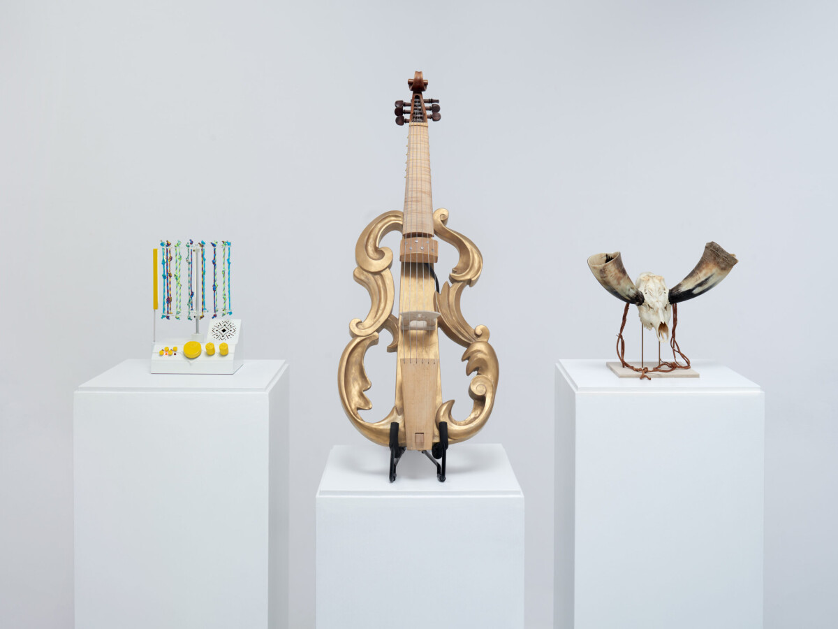 Three speculative designs on white pedestals with a white background. A quipu-powered drum machine with knotted pieces of rope, a viola da gamba with a hollow body and amplification, and a skull-and-bone horn.