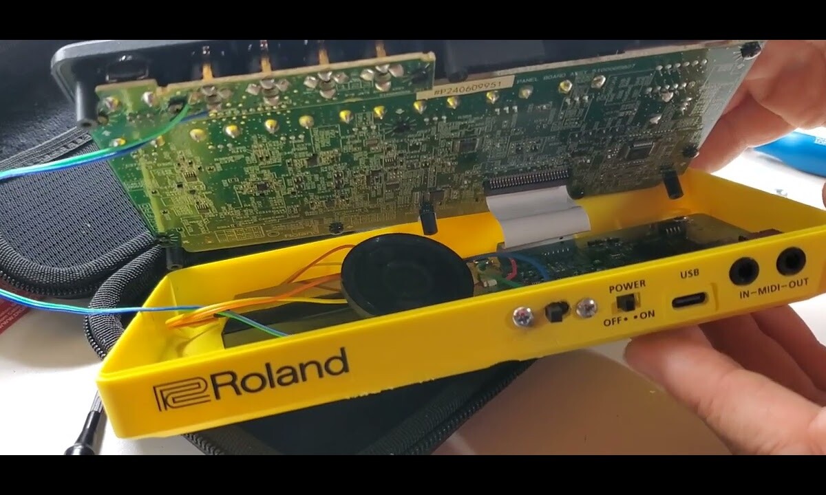 The yellow plastic case of a Roland P-6 pocket drum machine opened up, revealing the factory PCB board and mods with speaker and amplifier circuit.