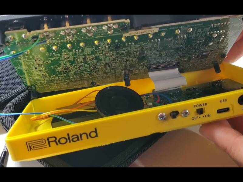 The yellow plastic case of a Roland P-6 pocket drum machine opened up, revealing the factory PCB board and mods with speaker and amplifier circuit.