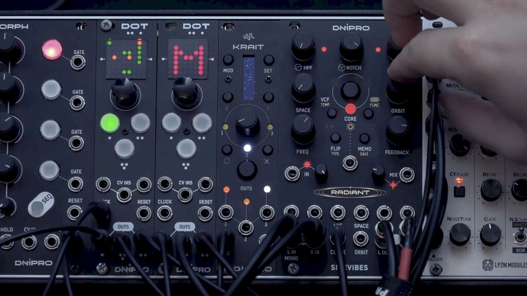 Dnipro Modular's Radiant sits alongside Morph, Dot, and Krait modules from the same maker, as a finger reaches out to grab the orbit knob, and a center CORE button is lit red amidst a radial layout of controls.