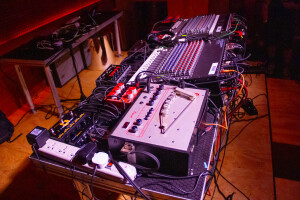 A table of electronic music gear including a tape delay, two mixers, and several effects pedals.