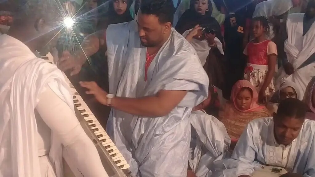 Ahmedou Ahmed Lowla plays an electronic keyboard turned on its side, his hands dancing across the keyboard, in a large crowd in Mauritania.