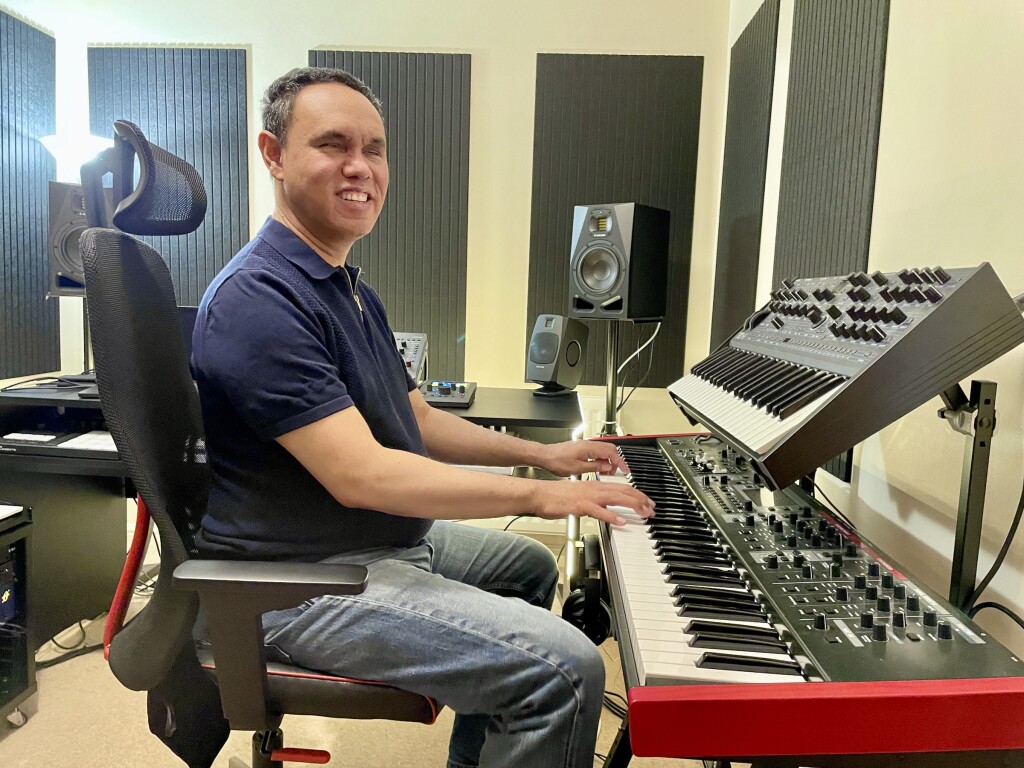 A smiling Jason sits at the studio, his hands on a Roland V-STAGE keyboard, studio monitors in the background.